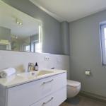 Badezimmer mit Waschbecken, Spiegel, Toilette und Fenster.