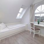 Schlafzimmer mit Dachschrägen, Bett, Schreibtisch und Fenster.