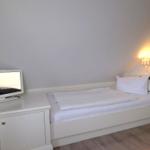 Schlafzimmer mit weißem Bett, Fernseher und Nachttisch unter schräger Decke.