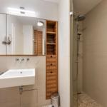 Bathroom with shower, sink, and wooden shelf.