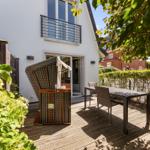 Terrace with table, chairs, and sunshade. Backyard with hedge and view of neighboring house.