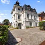 White villa with dark roof and cobblestone driveway. Entrance with sign Die Villa 1903.