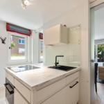 Kitchen with countertop, sink, and window. Passage to living area with sofa and trunk.