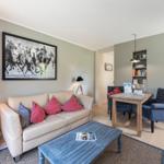 Living area with sofa, coffee table, and dining area. Wall art shows polo players.