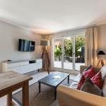 Living room with sofa, coffee table, and TV. Access to terrace with view of greenery.