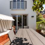 Terrace with wooden table, lounge chair, and glass doors to the apartment.