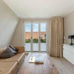 Wohnzimmer mit Sofa, Couchtisch und TV. Balkon mit Blick auf Gebäude.
