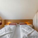Zimmer mit Doppelbett, Holz-Kopfteil, Nachttischen und Kleiderschrank unter schrägem Dach.