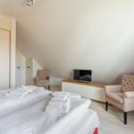 Schlafzimmer mit Doppelbett, zwei Sesseln, Fernseher und Kleiderschrank.