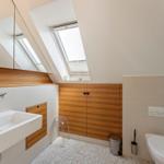 Badezimmer mit Dachfenster, Waschbecken, Toilette und Holzverkleidung.