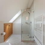 Badezimmer mit Dusche, Heizkörper und Holzschränken unter Dachschrägen.