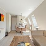 Wohn- und Essbereich mit Sofa, Tisch und Stühlen. Dachfenster und Fernseher sichtbar.