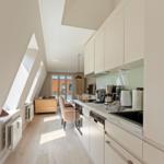 Küche mit Arbeitsfläche, Spüle und Geräten. Blick in Wohnbereich mit Sofa und Fenster.