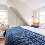 Schlafzimmer mit Dachschräge, Bett mit blauer Decke und Fenster mit Sitzbank.