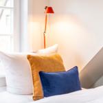 Ein Bett mit Kissen und einer Stehlampe neben einem Fenster.