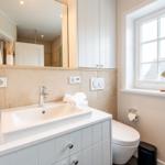 Badezimmer mit Waschbecken, Spiegel, Toilette und Fenster.