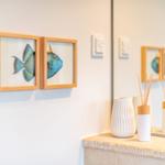 Zwei Bilder mit Fischen hängen an der Wand neben einem Spiegel mit Aromalampe.