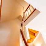 Treppe mit Holzgeländer und weißen Wänden, beleuchtet von Deckenleuchten.