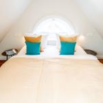 Schlafzimmer mit Dachschrägen, Bett mit Kissen und runden Nachttischen.