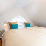 Schlafzimmer mit Dachschrägen, runden Fenster und Bett mit Kissen.