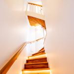 Holzgetreppe mit beleuchteten Stufen und Geländer führt nach oben.