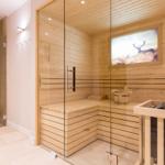 Sauna mit Holzbank und Glaswand. Dampfdusche daneben. Wandbild mit Hirsch.