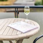 Runder Holztisch auf Balkon mit Glas Weißwein und Magazin.