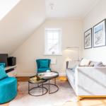 Wohnzimmer mit Sofa, zwei blauen Sesseln, Tisch und Fenster unter Dachschräge.