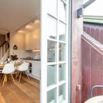 Ein Essbereich mit Tisch, Stühlen und Küchenzeile. Durchgehendes Holzparkett und eine Treppe sind sichtbar.