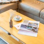 Holztisch mit Kaffeetasse, Zeitschrift und Trockenblumen vor einem Ledersofa.