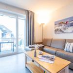 Wohnzimmer mit Sofa, Tisch und Balkonansicht. Wandbild zeigt Windsurfer.