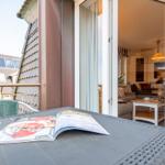 Terrasse mit Tisch, Stuhl und Wein. Blick ins Wohnzimmer mit Sofa und Tisch.