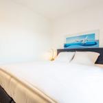 Schlafzimmer mit Bett, Nachttisch und Wandbild mit Segelboot.