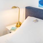 Schlafzimmer mit Bett, Nachttisch und goldener Lampe.