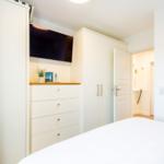 Schlafzimmer mit weißem Bett, Kleiderschränken und Fernseher an der Wand.