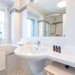 Badezimmer mit Waschbecken, Spiegel, Dusche und Fenster mit Pflanze.