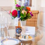 Tisch mit Blumen, Wein und Tassen auf Glasplatte.