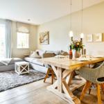 Dining area with wooden table and chairs. Living area with sofa and glass door. Wall decor and flowers.