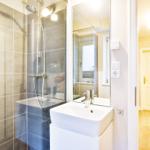 Bathroom with shower, sink, and mirror. Wooden floor and door visible in hallway.