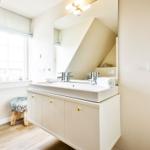 Bathroom with sink, mirror and window. Wooden floor and stool with fur cover.