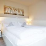 A bed with white linens, two nightstands with lamps, and a wall painting with sailboats.