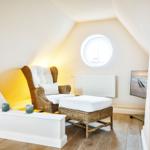 A bedroom with rattan armchair, round window and wooden floor.