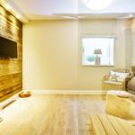 Room with wooden wall, TV, window and chair. Wooden floor and ceiling light.