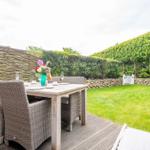 Rear yard with wooden deck, garden table, chairs, and green lawn.