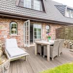 Deck with table, chairs, and lounge. House with brick wall and dormer windows.