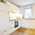 Kitchen with white cabinets, wooden floor, and window with roller blind.