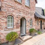 Two-story brick house with entrance door and windows. Plants in baskets near the entrance.