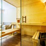 Sauna with wooden bench and glass wall. Chairs and a window are visible in the background.