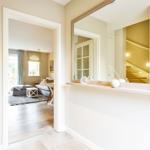 Hallway with mirror, tile floor, and view into living room with sofa and windows.