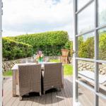 Deck with table, chairs, and lounge, surrounded by greenery and stone walls.